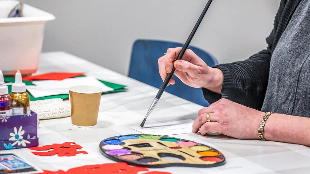 Nainen maalaamassa vesiväreillä pöydän ääressä.