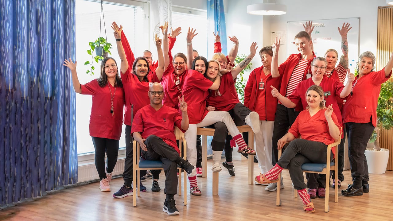 Ryhmäkuva Esperin iloisista hoitajista, joilla on päällään punaiset paidat ja jotka ovat nostaneet kätensä ilmaan