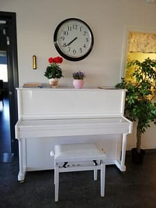 Hoivakodin valkoinen piano, jonka päällä on seinäkello.