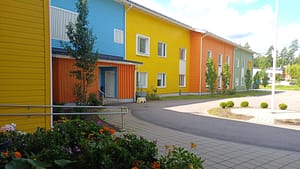 Esperi Hoivakoti Harjuksen rakennus, jonka julkisivu on maalattu sinisen, keltaisen, oranssin ja vihreän eri sävyihin, edessä kukkaistutus ja käytävä pihalle.