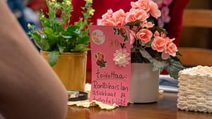 Asukkaalle tehty vaaleanpunainen 90-vuotissyntymäpäiväkortti pöydällä nojaamassa kukkia vasten.