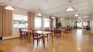 Iso ruokailutila, useita pöytiä ja tuoleja sekä näkymä viereiseen oleskelutilaan.