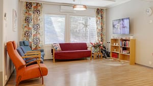 Tilava oleskeluhuone, sohva, nojatuoleja ja televisio seinällä.