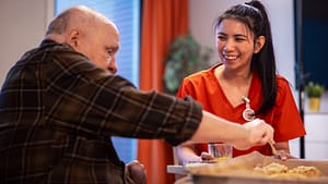 Hoitaja seurustelee asukkaan kanssa leivontatilanteessa hoivakodissa.