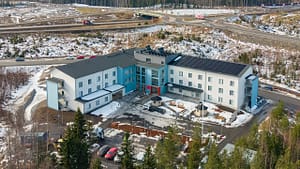 Ilmakuva kodista Kangasalla talvimaisemassa, rakennus metsän ja tieverkoston ympäröimänä.