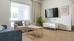 Viihtyisä oleskeluhuone, jossa nojatuoleja, sohva, televisio ja vaalea sisustus.