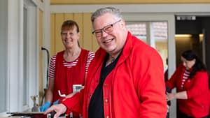 Villa Fredrikan hoivakodin yksikönpäällikkö hymyilee ulkotapahtumassa muun henkilökunnan seurassa. Kuvassa valmistellaan tarjoiluja yhteiseen hetkeen.