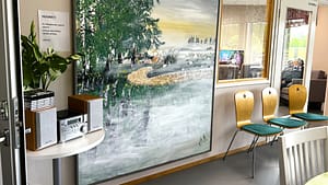 Yhteistilan seinällä oleva luontoaiheinen taideteos ja sen ympärillä oleva rauhallinen sisustus.