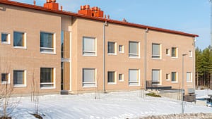 Rakennuksen julkisivu aurinkoisessa talvimaisemassa.