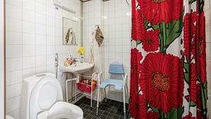Esteetön kylpyhuone, wc-istuin, suihku ja suihkutuoli, värikäs suihkuverho.