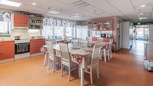 Tilava keittiö ja ruokailutila, useita pöytiä ja tuoleja, kodinkoneet ja kaapistot.
