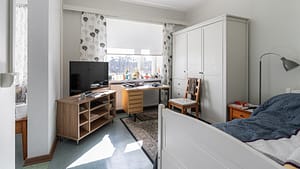 Yksinkertainen makuuhuone, sänky, vaatekaappi, työpöytä ja televisio.