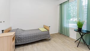 Asukkaan huone, jossa sänky ja yöpöytä vaaleassa tilassa.