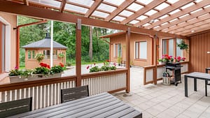 Puinen pergola terassilla, reunoilla kukkivia istutuksia.