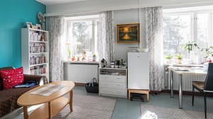 Kodikas huone, sohva, sohvapöytä, kirjahylly ja työpiste.