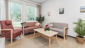 Oleskelutila, jossa harmaa sohva ja pöytä, ikkunasta näkymä kukkivalle terassille.
