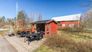 Katettu terassi rakennuksen sisäänkäynnin yhteydessä, kaksi tuolia, pieni pöytä ja nojatuoli.