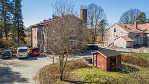 Kaksikerroksinen vaalea asuinrakennus, piha-alue ja pysäköityjä autoja.
