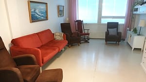 Hoivakodin oleskelutila, jossa tuoleja, sohva ja tauluja.