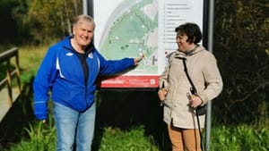 Kaksi henkilöä seisoo kartan edessä ulkona.