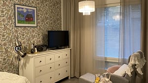 Huoneen nurkkaus, jossa on seinässä kuviollinen tapetti, TV ja huonekaluja.