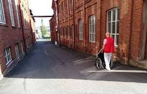 Hoivakodin työntekijä työntämässä ihmistä rollaattorissa.