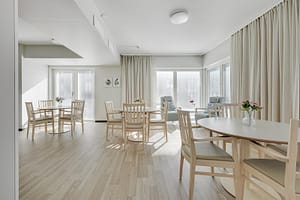 Yhteinen ruokailutila, jossa useita pöytäryhmiä ja suuret ikkunat.