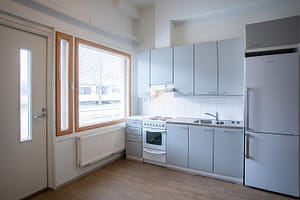 Tyhjä, valoisa huone jossa keittiökalusteita.