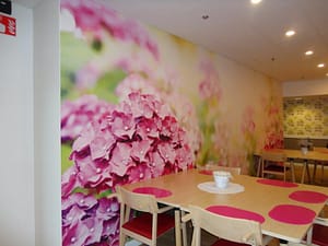 Hoivakodin huone, jossa näkyy kukkakuvioisen seinän edessä pöytä ja tuoleja.