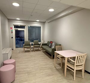 Yhteinen oleskelutila, jossa vihreä sohva, kaksi tuolia, pieni ruokapöytä ja ovi ulos terassille.