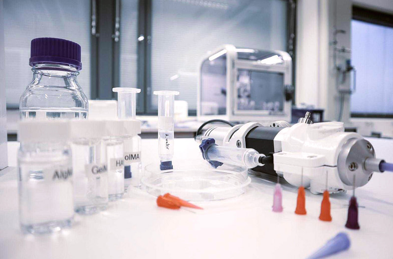 Tutkimustyöhön käytettäviä välineitä pöydällä. Taustalla biotulostin.