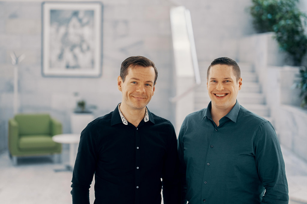 Two men standing side by side at an office building lobby.