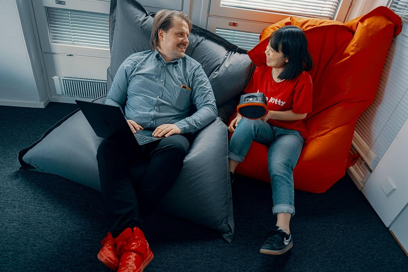 A man and a woman sitting in bean bag chairs, holding a laptop and an acoustic camera, and smiling.