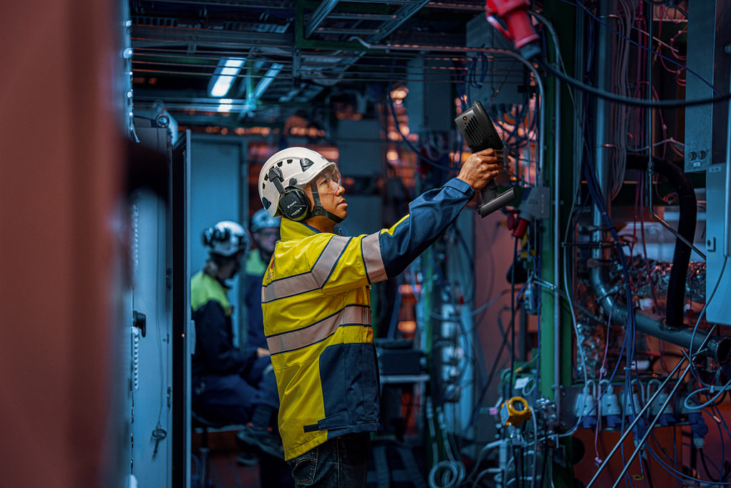 Man standing in an industrial environment and pointing an acoustic camera to detect air and gas leaks.