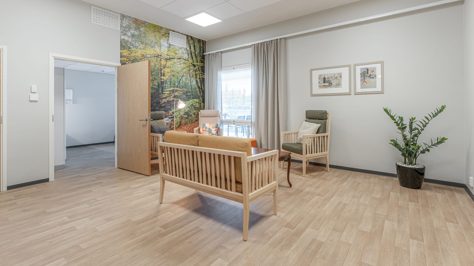 Viihtyisä oleskelutila, jossa nojatuoleja, sohva ja metsäaiheinen seinä Lamminrahkan hoivakodissa Kangasalla.