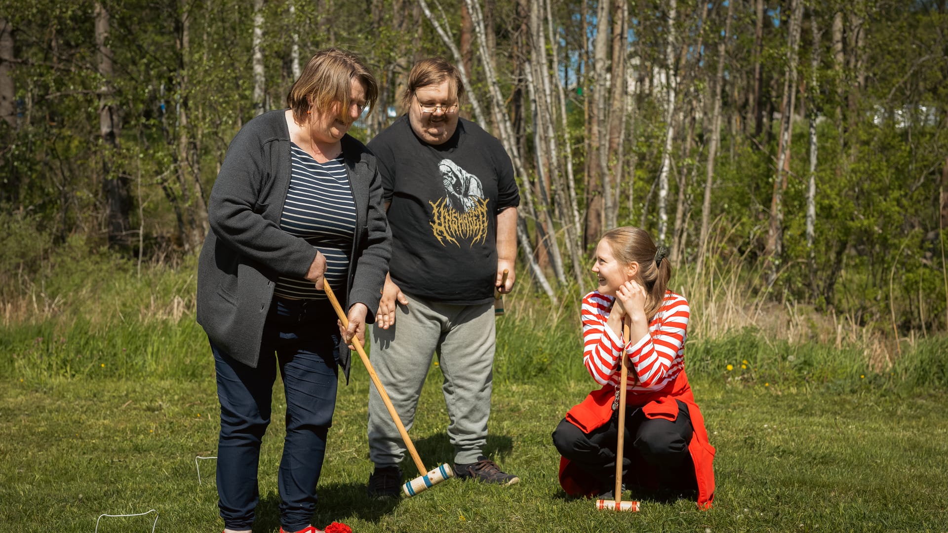 Esperi Koti Sypressin asukkaat pelaavat mailapeliä ohjaajan kanssa ulkona kesäisessä maisemassa.
