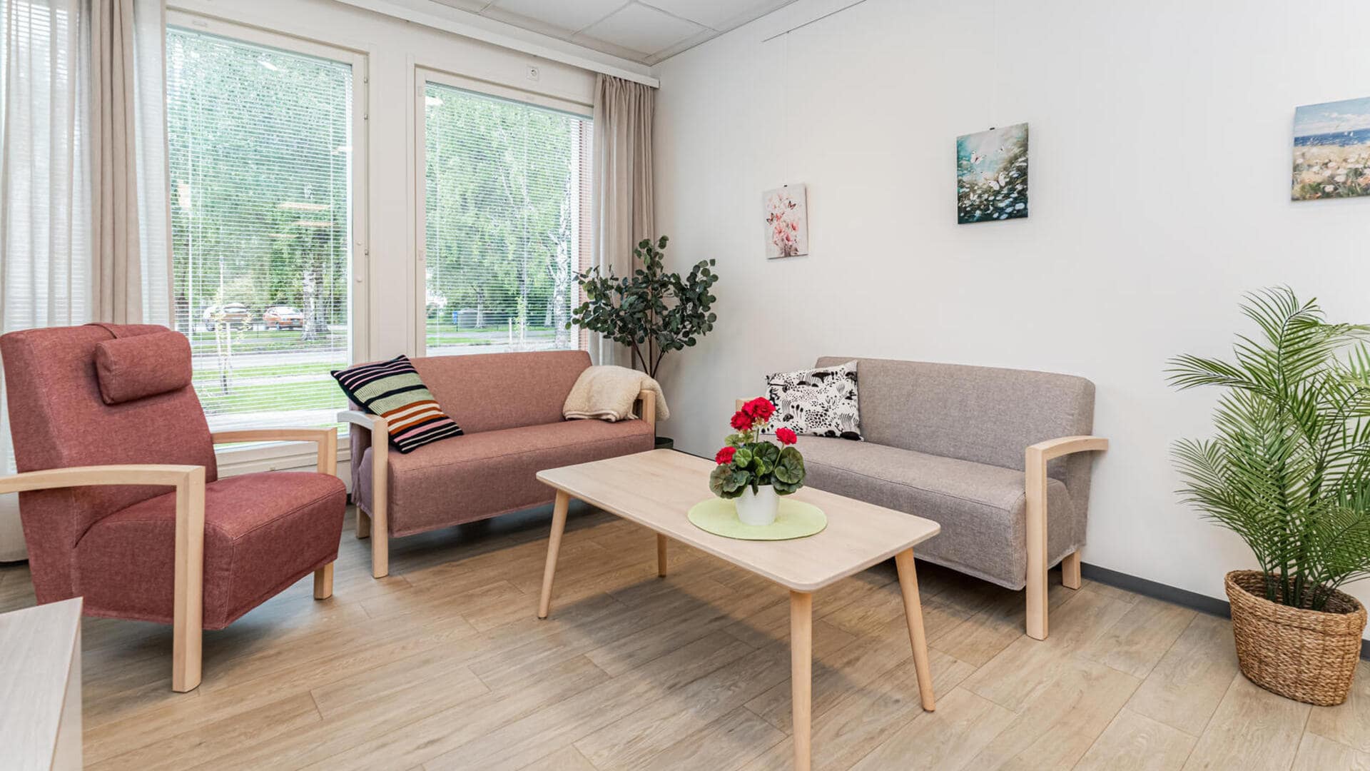 Oleskelutila, jossa harmaa sohva ja pöytä, ikkunasta näkymä kukkivalle terassille.