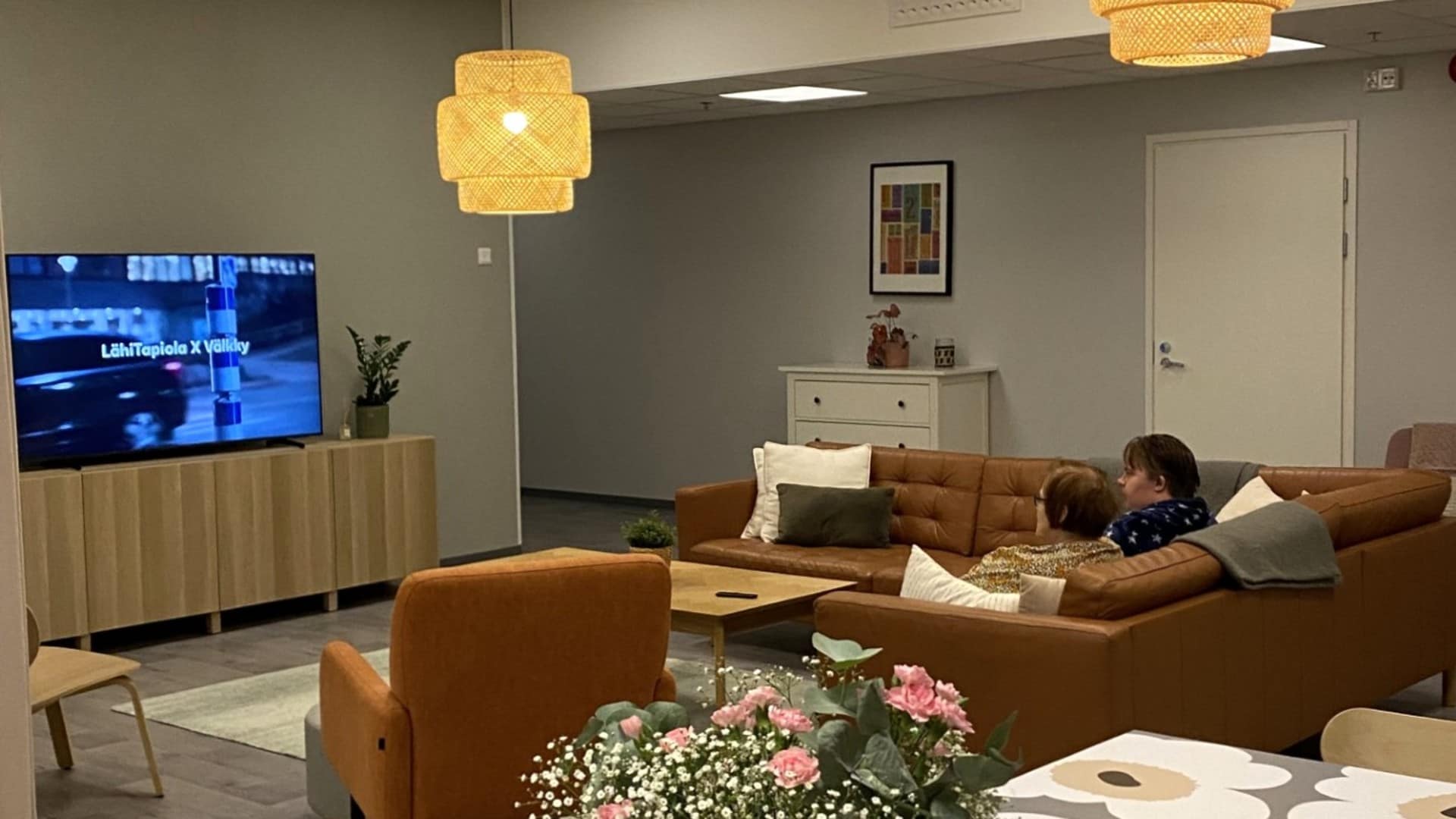 Asukkaita katselemassa televisiota kodikkaasti sisustetussa olohuoneessa.