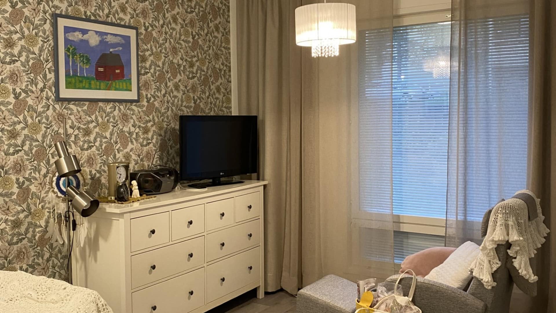 Huoneen nurkkaus, jossa on seinässä kuviollinen tapetti, TV ja huonekaluja.