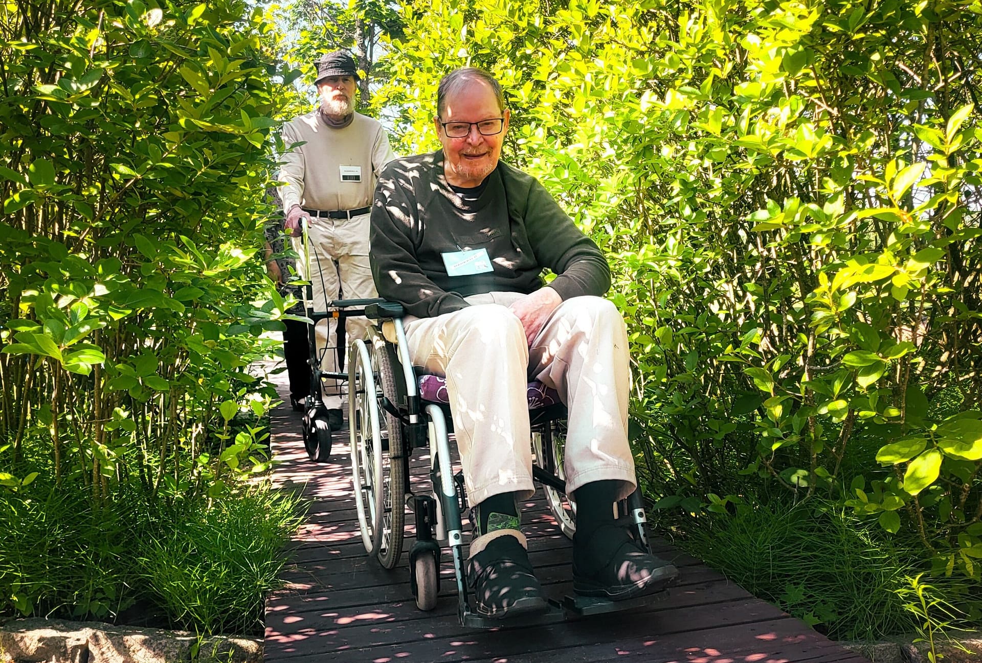 Asiakas pyörätuolissa ulkoilemassa vehreällä pihapolulla