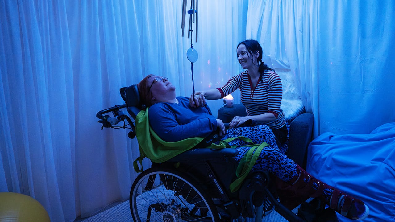 Vammaispalvelun asukas ja hoitaja sinisävyisessä, hämärässä aistihuoneessa