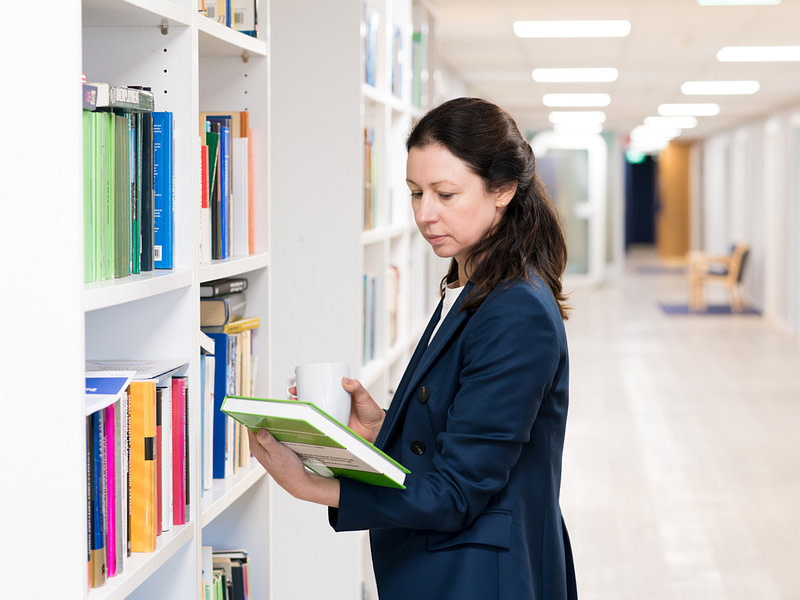 Natalia Kuosmanen tutkii kirjaa kirjahyllyn edessä.