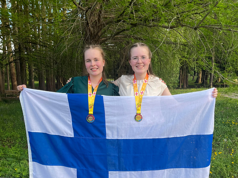 Siiri Roschier ja Aino Alanko voittivat prossia ja kultaa Euroopan tyttöjen matematiikan olympialaisissa. Kuvassa Siiri ja Aino mitaliensa ja Suomen lipun kanssa.